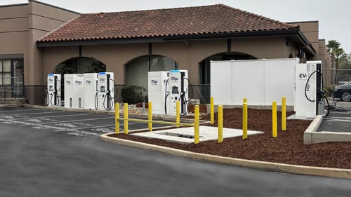 Several EVgo fast-charging units installed in marked parking spaces at a public charging station, with EVgo logos on the chargers, protective bollards around each unit